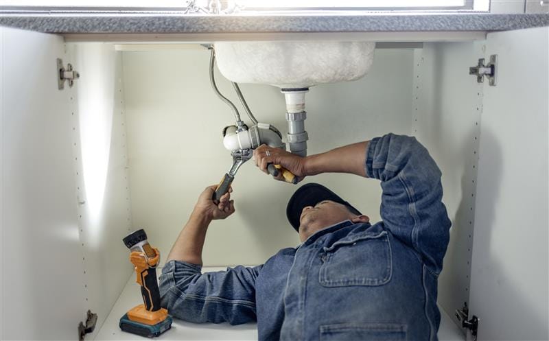Plumber repairing pipes beneath a bathroom sink in Warminster