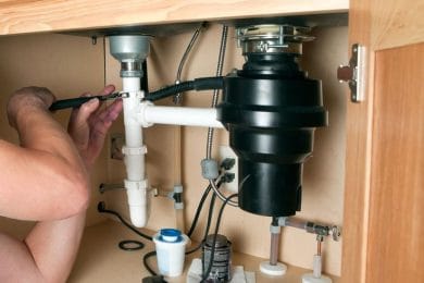 Plumber repairing a garbage disposal beneath a kitchen sink in Warminster