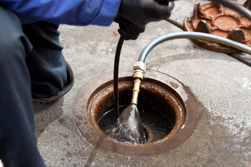 Plumber hydro jetting a sewer line through a manhole in Warminster