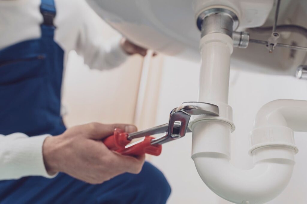 Plumber repairing a white drain pipe beneath a sink in Warminster