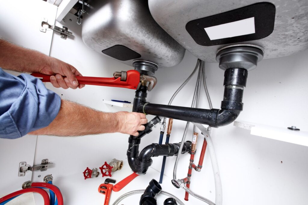 Plumber repairing drain pipes beneath a kitchen sink in Warminster